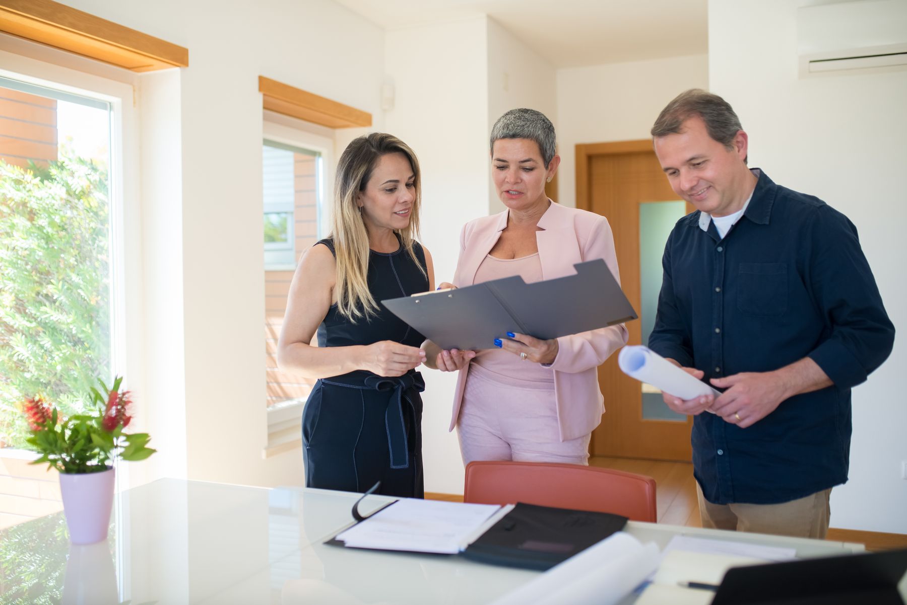 Real estate professional reviewing property documents with two clients inside a bright home